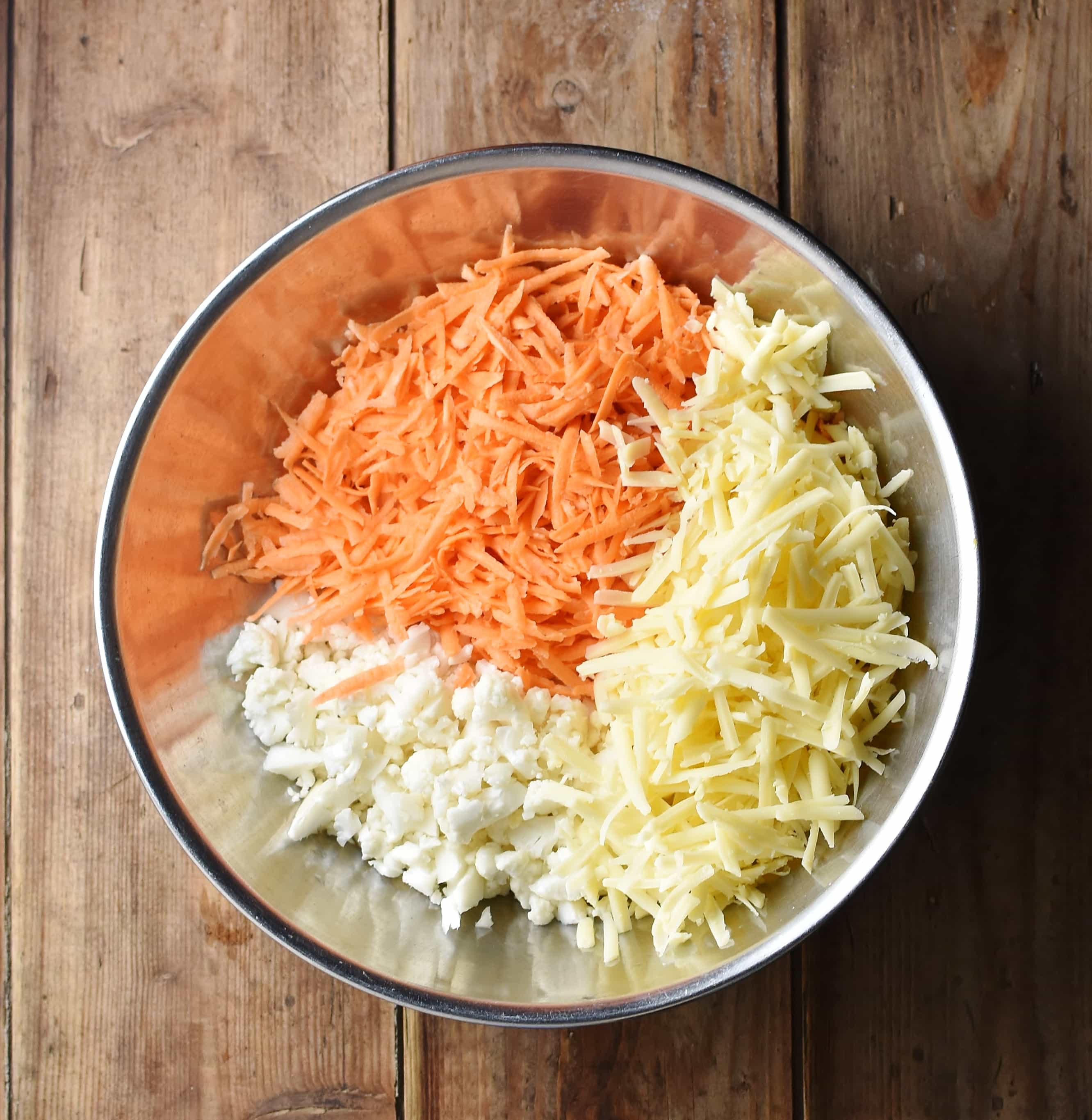 Grated sweet potato, cheese and chopped cauliflower in large metal bowl.