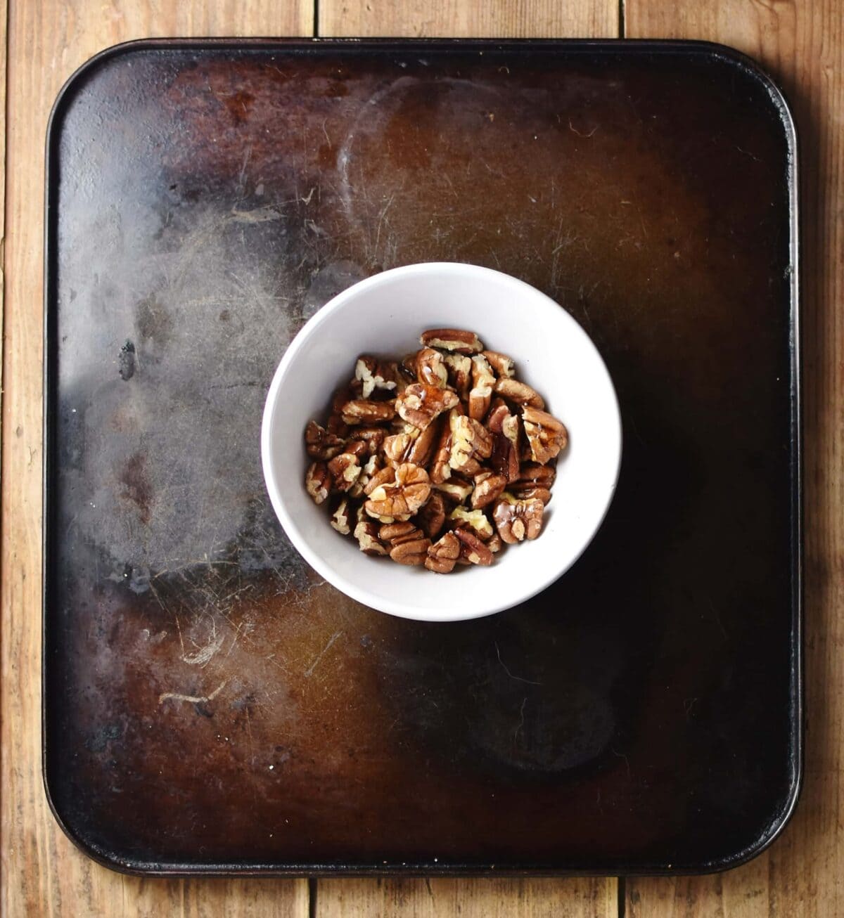 Chopped pecan nuts with maple syrup in small white bowl.