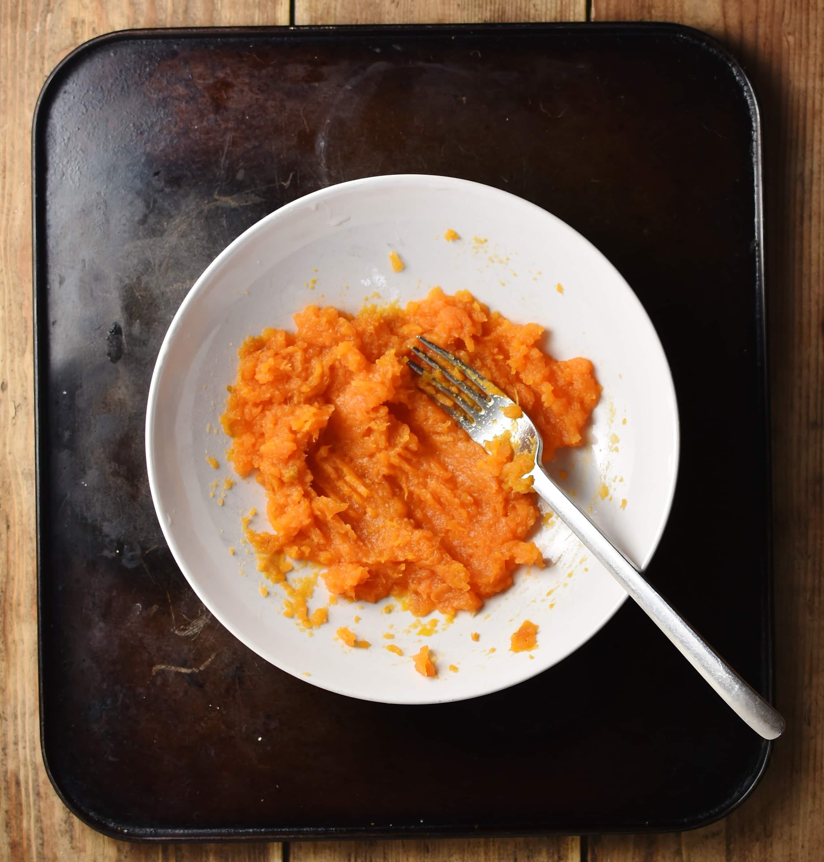 Top down view of mashed sweet potato in white bowl with fork.