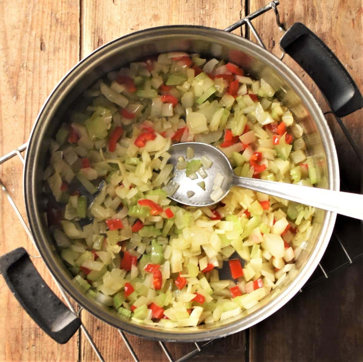 Stewed onion, celery and pepper in saucepan with spoon.