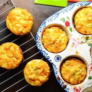 Top down view of sweet potato egg muffins in ceramic muffin dish and on top of cooling rack, with green spatula at top.