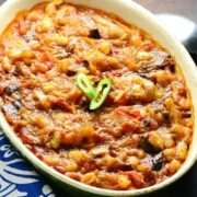 Eggplant in tomato sauce in white oval dish with spoon and blue-and-white cloth.