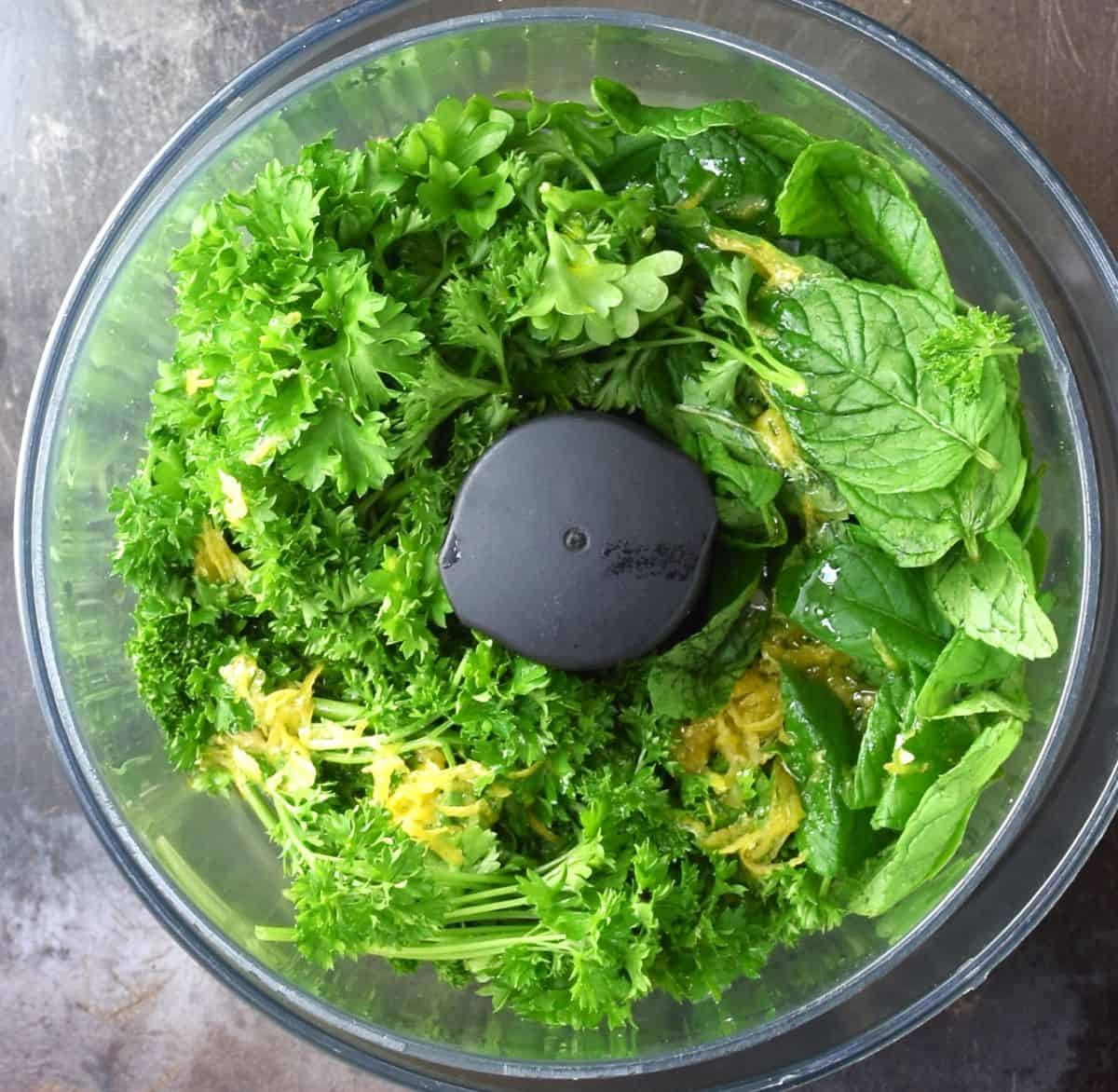 Fresh parsley stalks and mint leaves in food processor bowl.