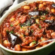 Side view of eggplant casserole with beans and rich tomato sauce in oval dish with spoon.