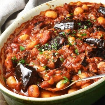 Side view of eggplant casserole with beans and rich tomato sauce in oval dish with spoon.