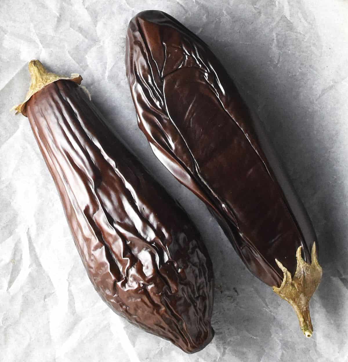 Top down down view of 2 whole roasted eggplants on parchment.