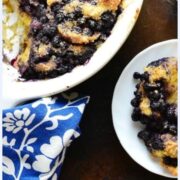 Top down partial view of blueberry french toast casserole in white dish and on white plate with blue-and-white cloth in bottom left corner.