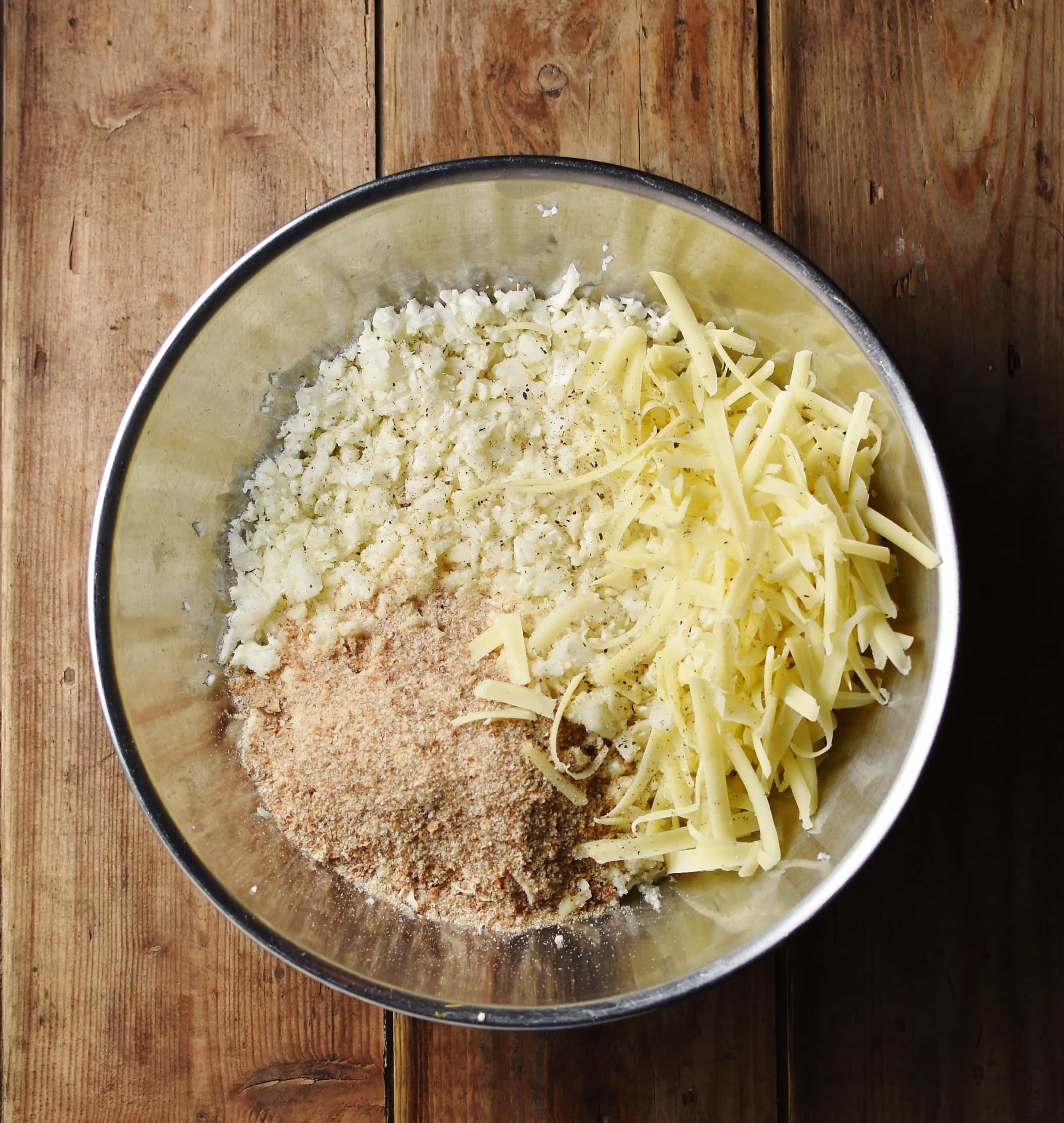 Cauliflower rice, grated cheese and breadcrumbs in large metal bowl.