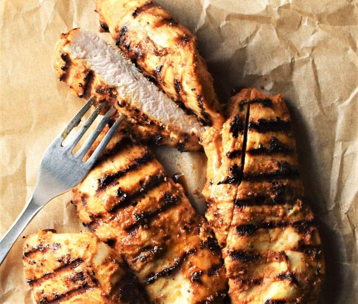 Grilled chicken breast pieces with fork on top of parchment.