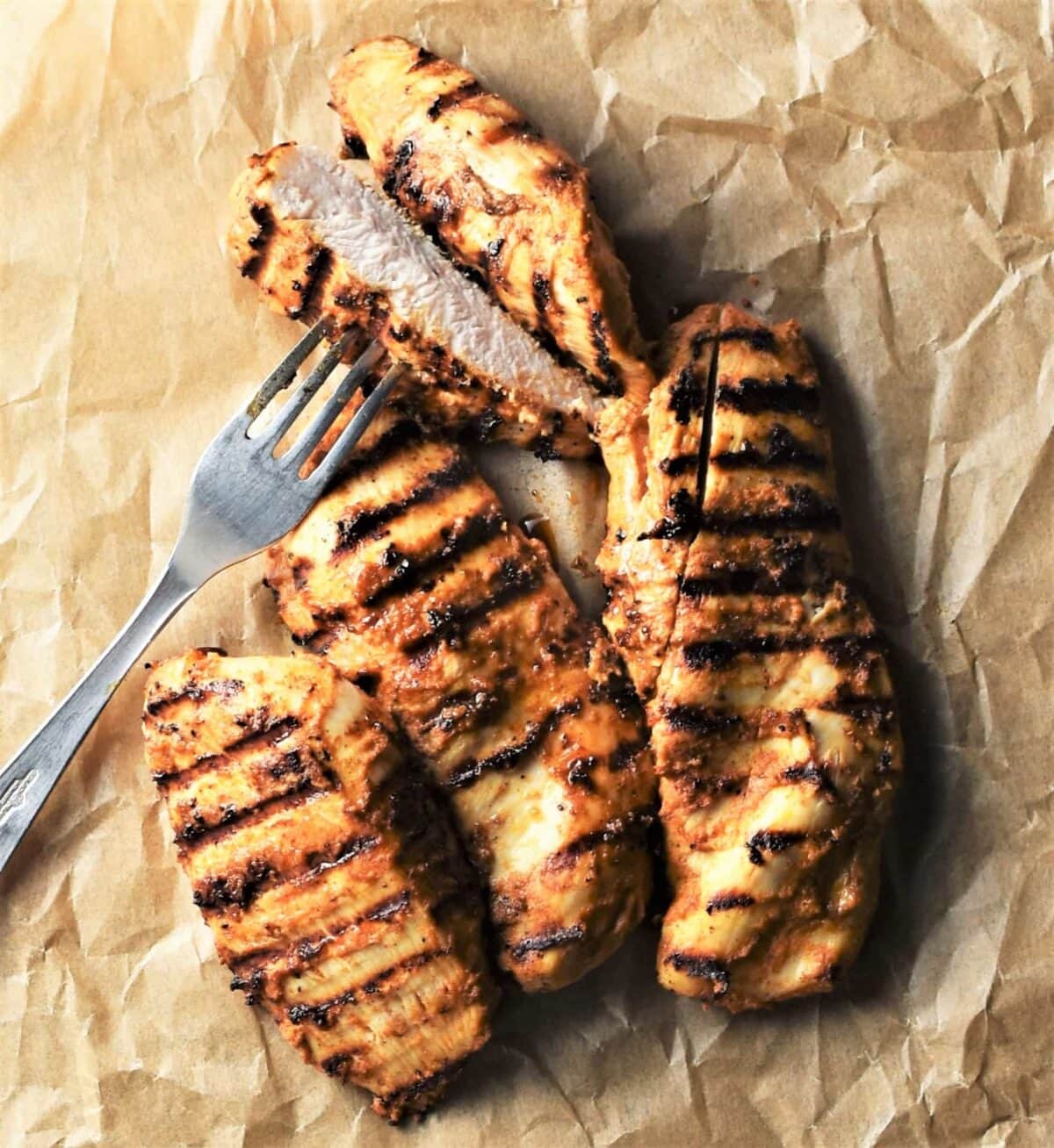 Grilled chicken pieces on top of parchment with fork.