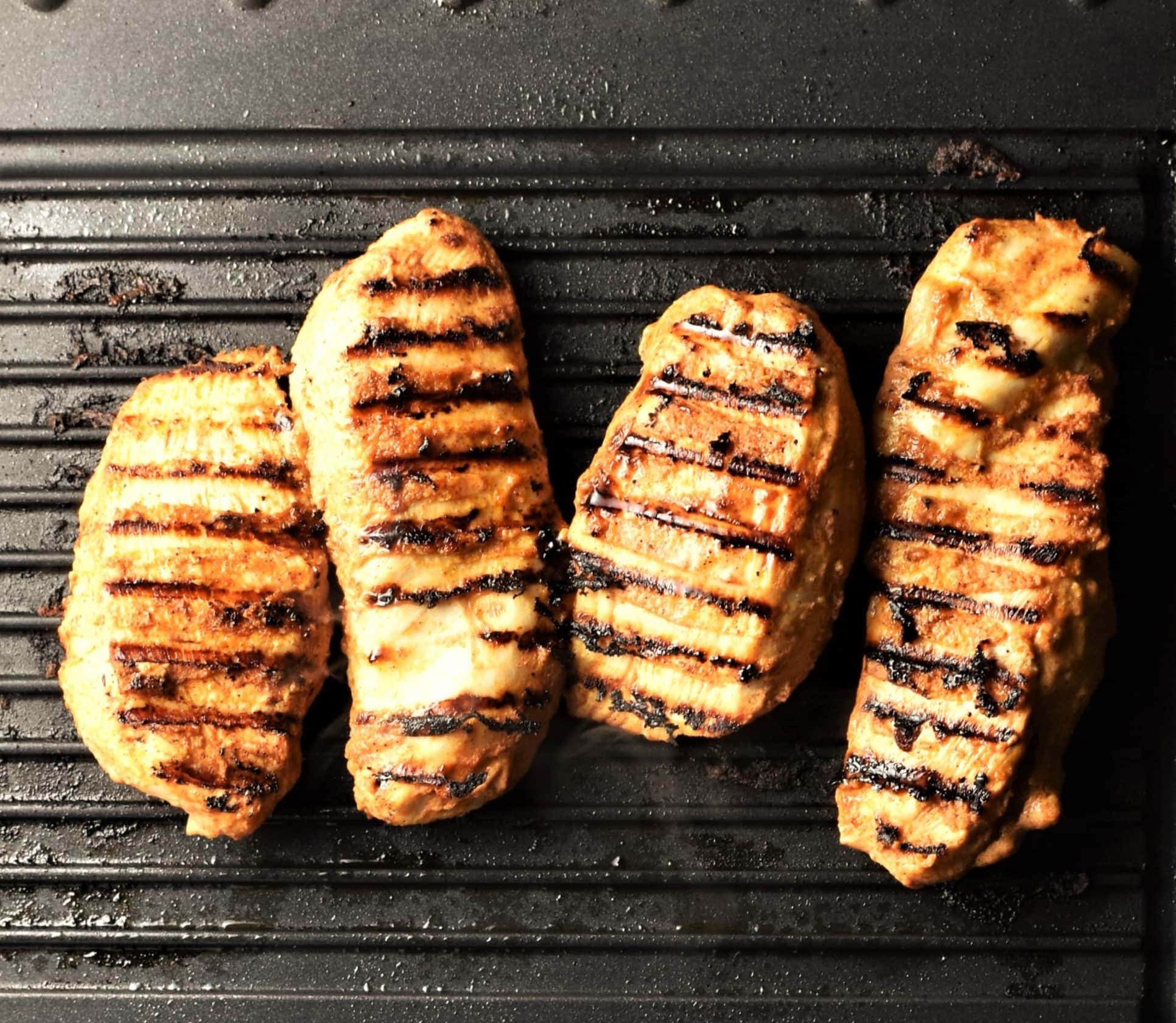 4 grilled chicken breast pieces on top of griddle pan.