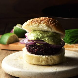 Side view of quinoa beet burger on top of marble plate with lime and chives in background.