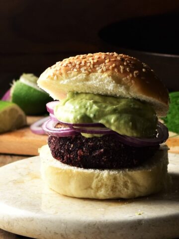 Side view of quinoa beet burger on top of marble plate with lime and chives in background.