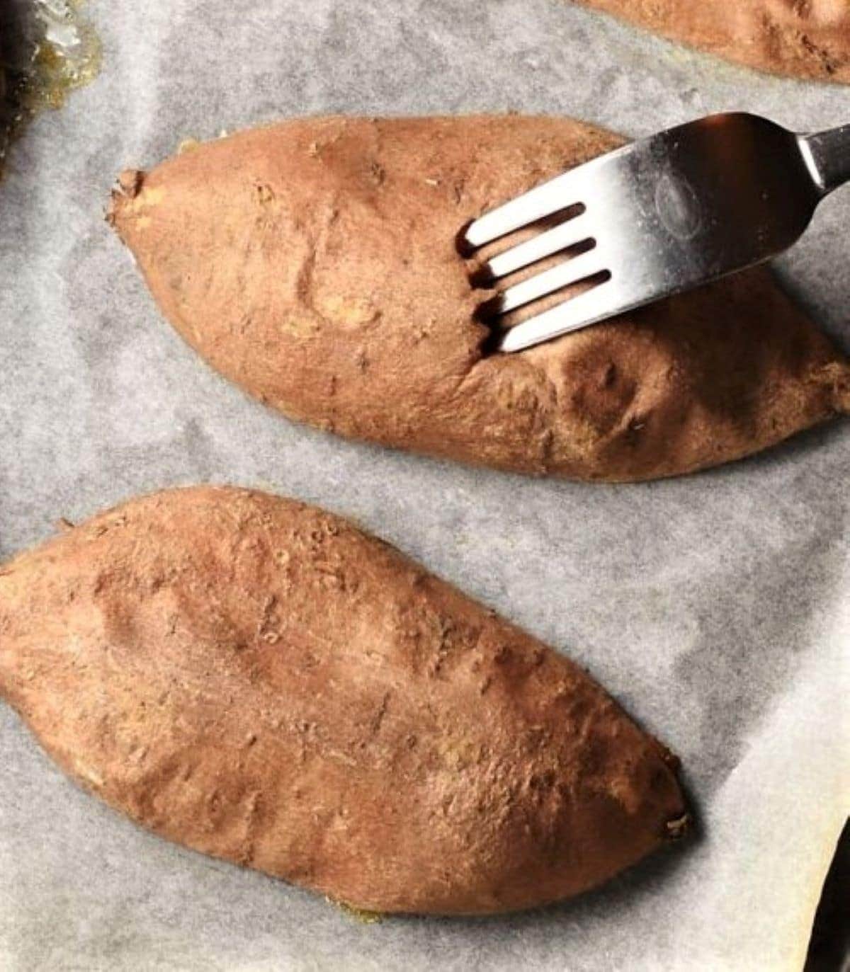 2 halves of sweet potato with fork on parchment.