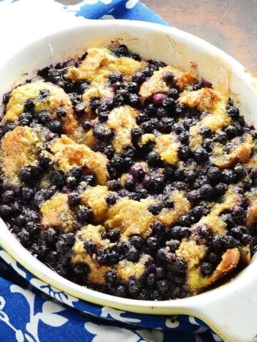 Blueberry french toast in white oval dish and blue-and-white cloth to left.