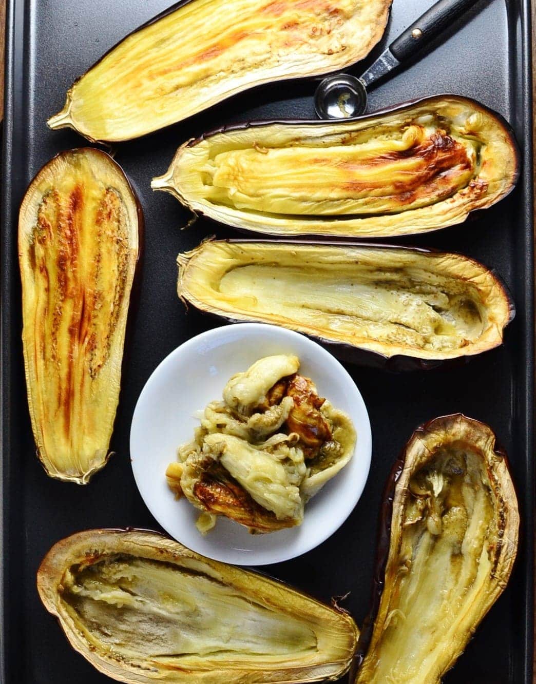 Eggplant halves on even tray with small white plate.