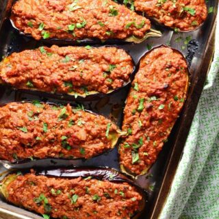 Top down view of stuffed eggplant on oven tray with green cloth.