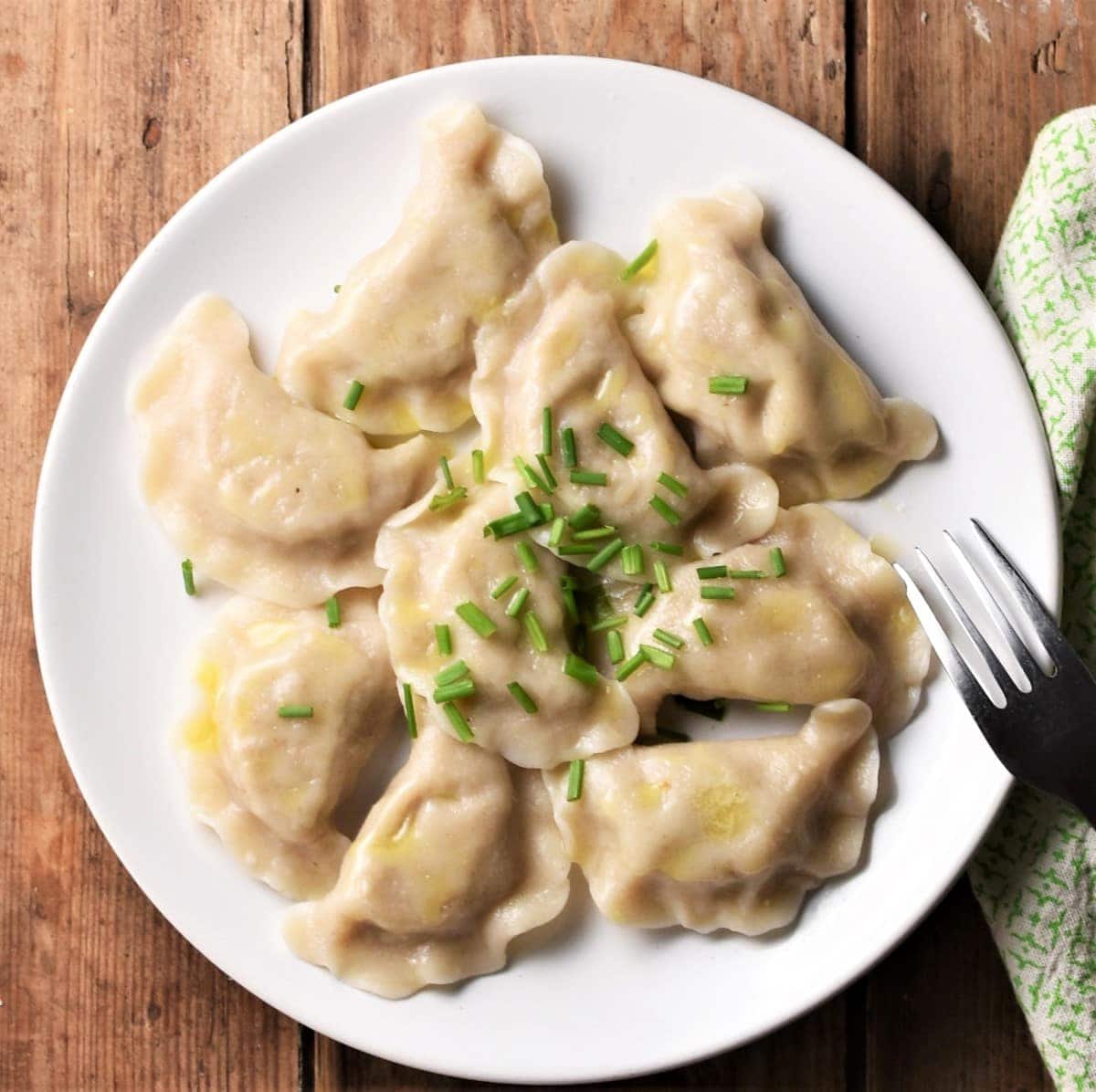 Pierogi with chives on top of plate.