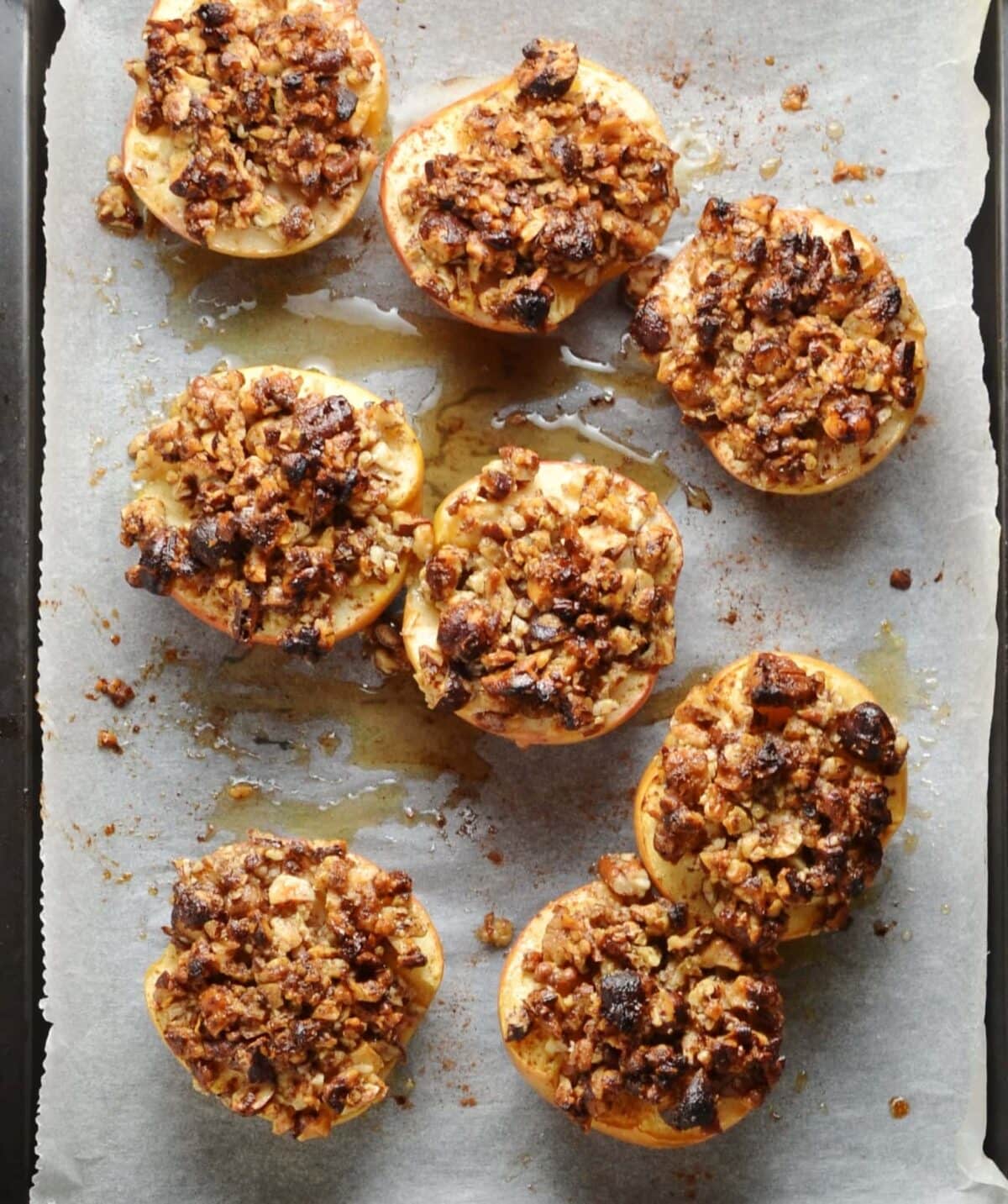 Baked apple halves with chopped pecans on top of paper.