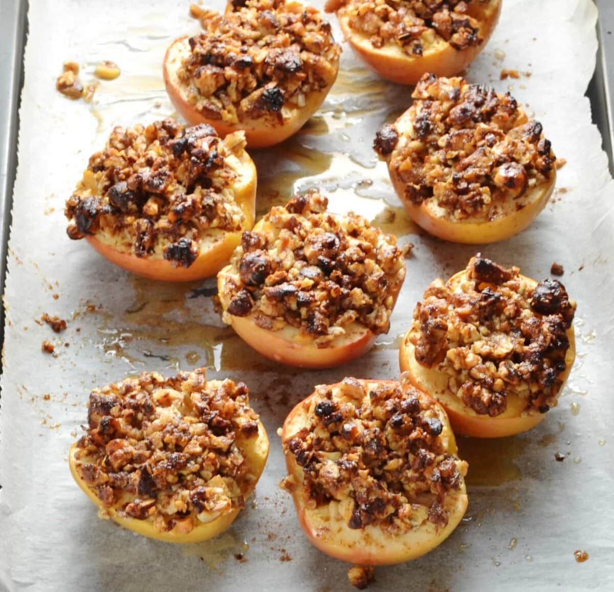 Apple halves with pecans pieces on top of baking paper.