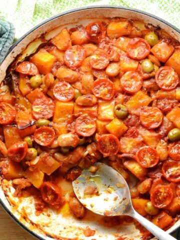 Top down view of butternut squash casserole in large shallow white dish with spoon and green cloth at top.