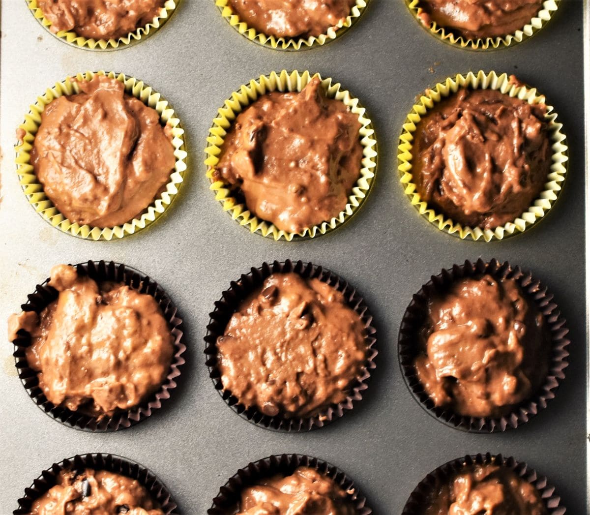 Pumpkin cocoa muffin batter in yellow and brown liners in muffin pan.