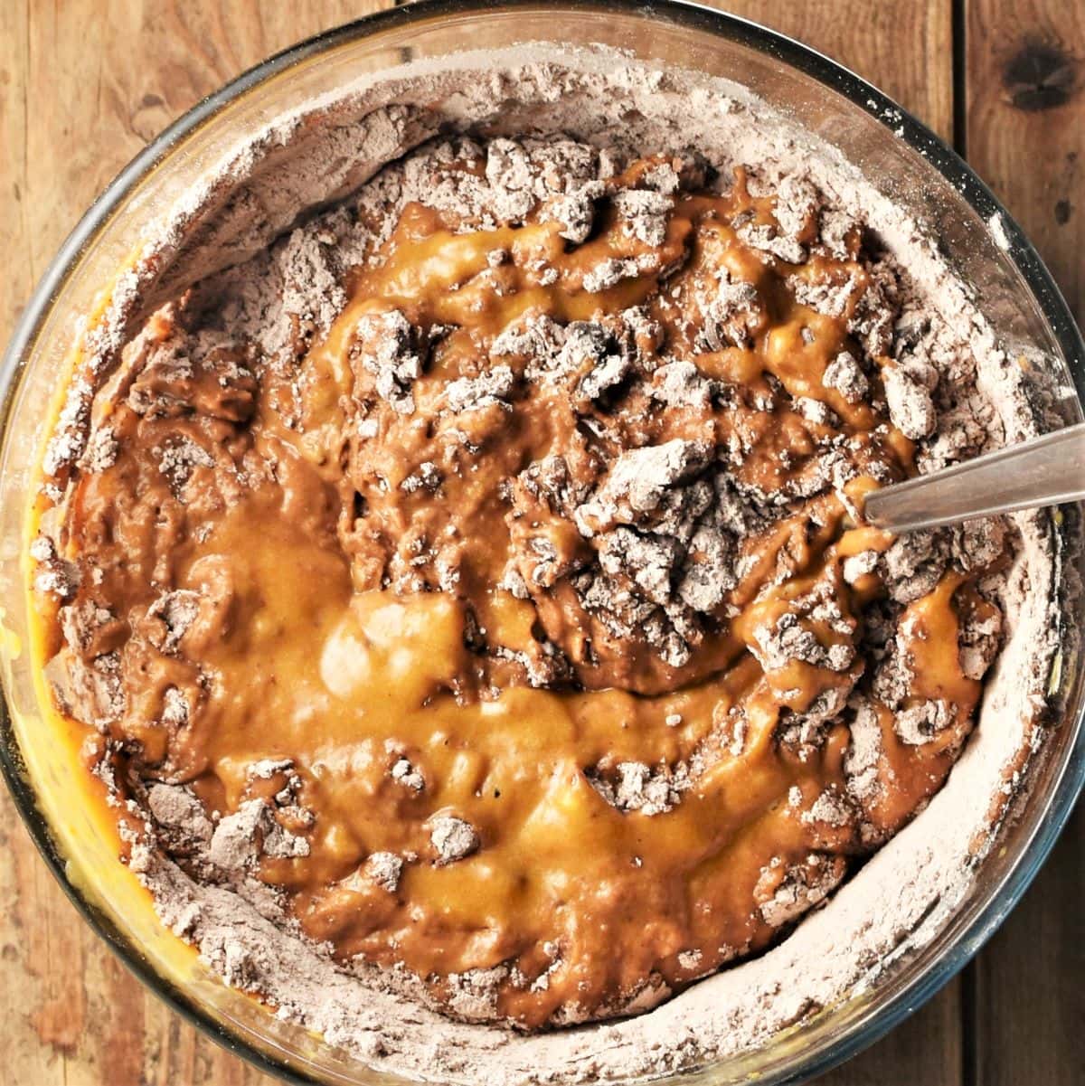 Pumpkin chocolate muffin batter in bowl with dry ingredients partly visible.