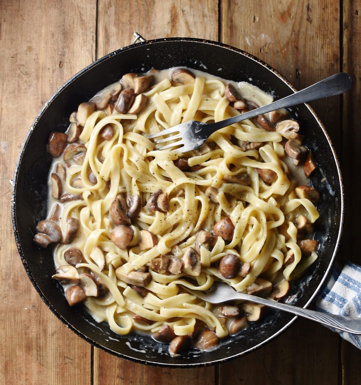 Tagliatelle pasta with mushroom sauce and 2 forks in large skillet.