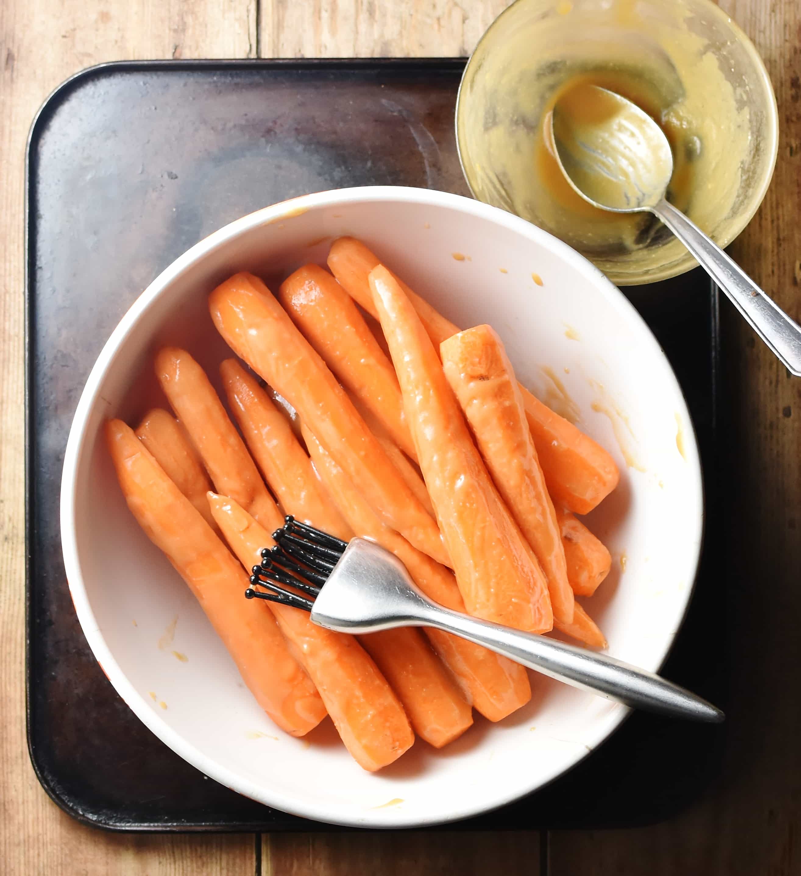 Peeled carrots with glaze in white bowl with pastry brush and miso glaze in small bowl with spoon in top right corner.