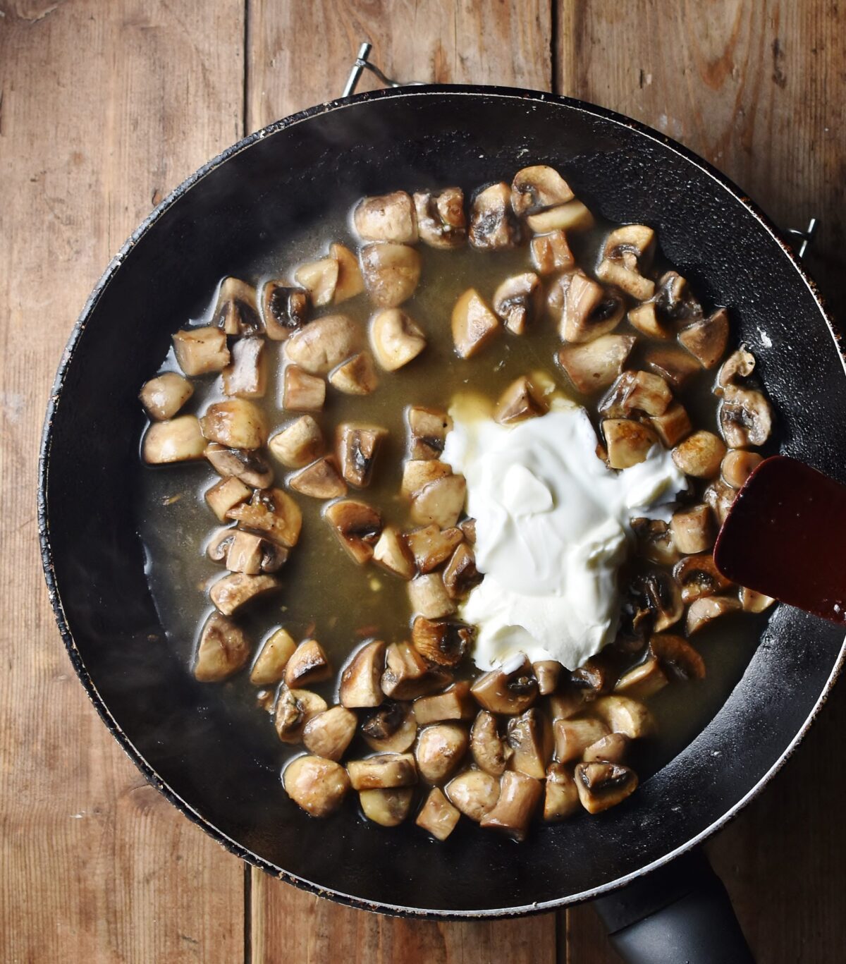 Chopped mushrooms with sauce and dollop of fromage frais in large pan.