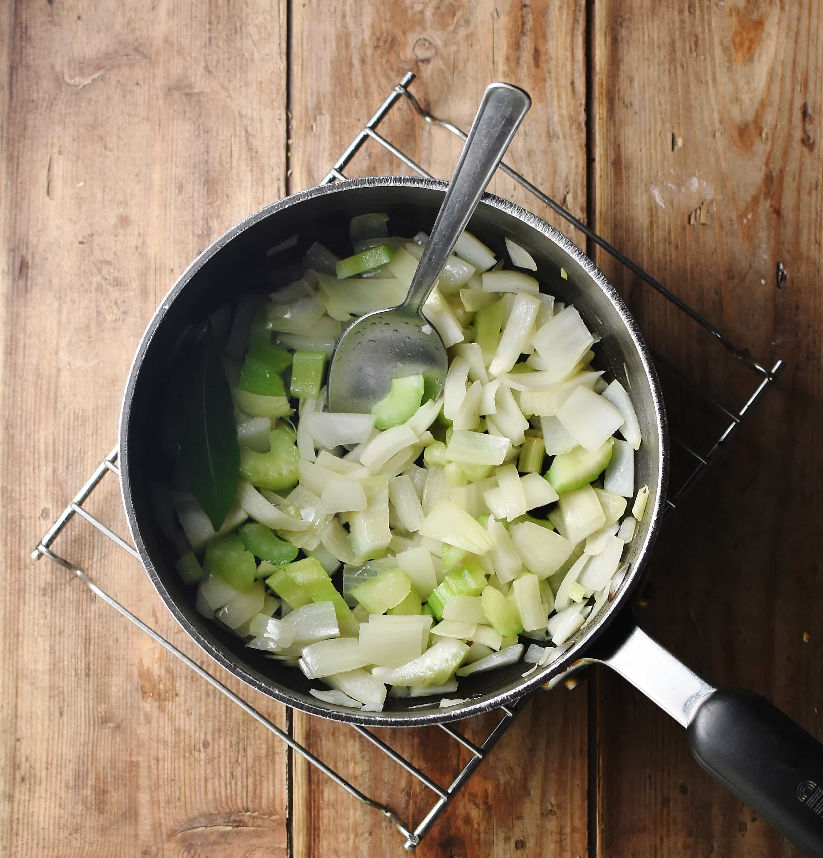 Chopped onion and celery in large pot with spoon.