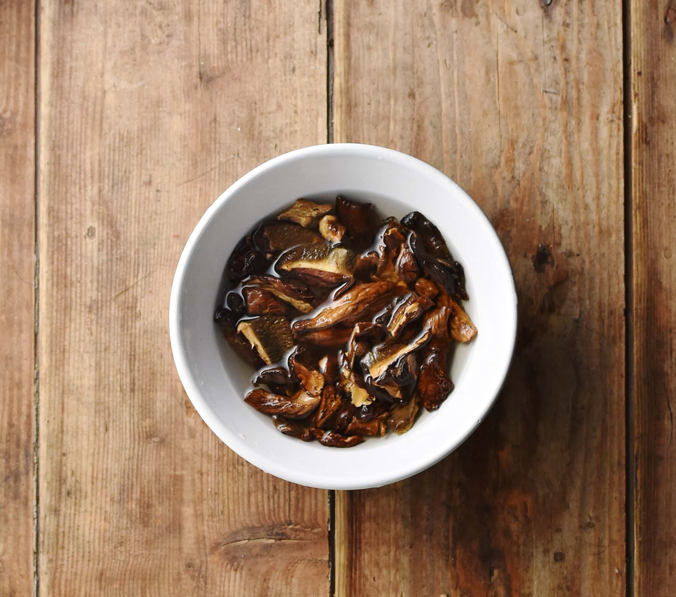 Dried porcini mushrooms in small white bowl with water.
