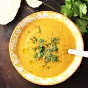 Top down view of creamy butternut squash lentil soup in yellow bowl with spoon.