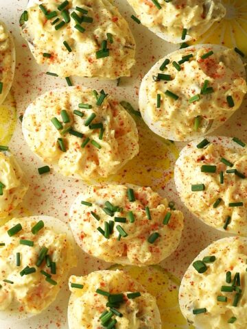 Top down view of potato salad deviled eggs with chives on yellow plate.