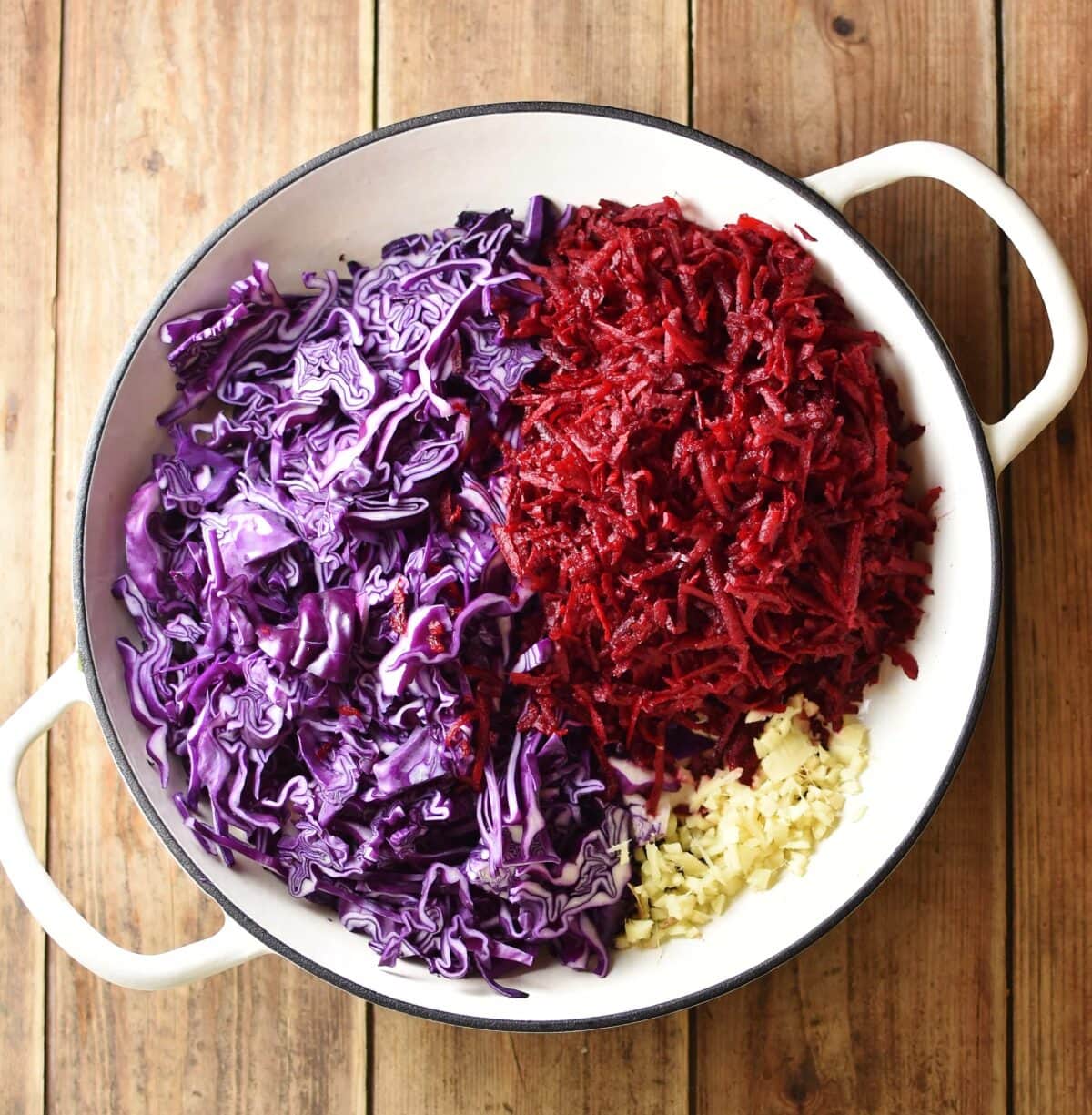 Shredded red cabbage, grated beetroot and chopped ginger in large white pan.