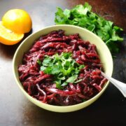 Braised red cabbage in yellow bowl with spoon and clementine in background.
