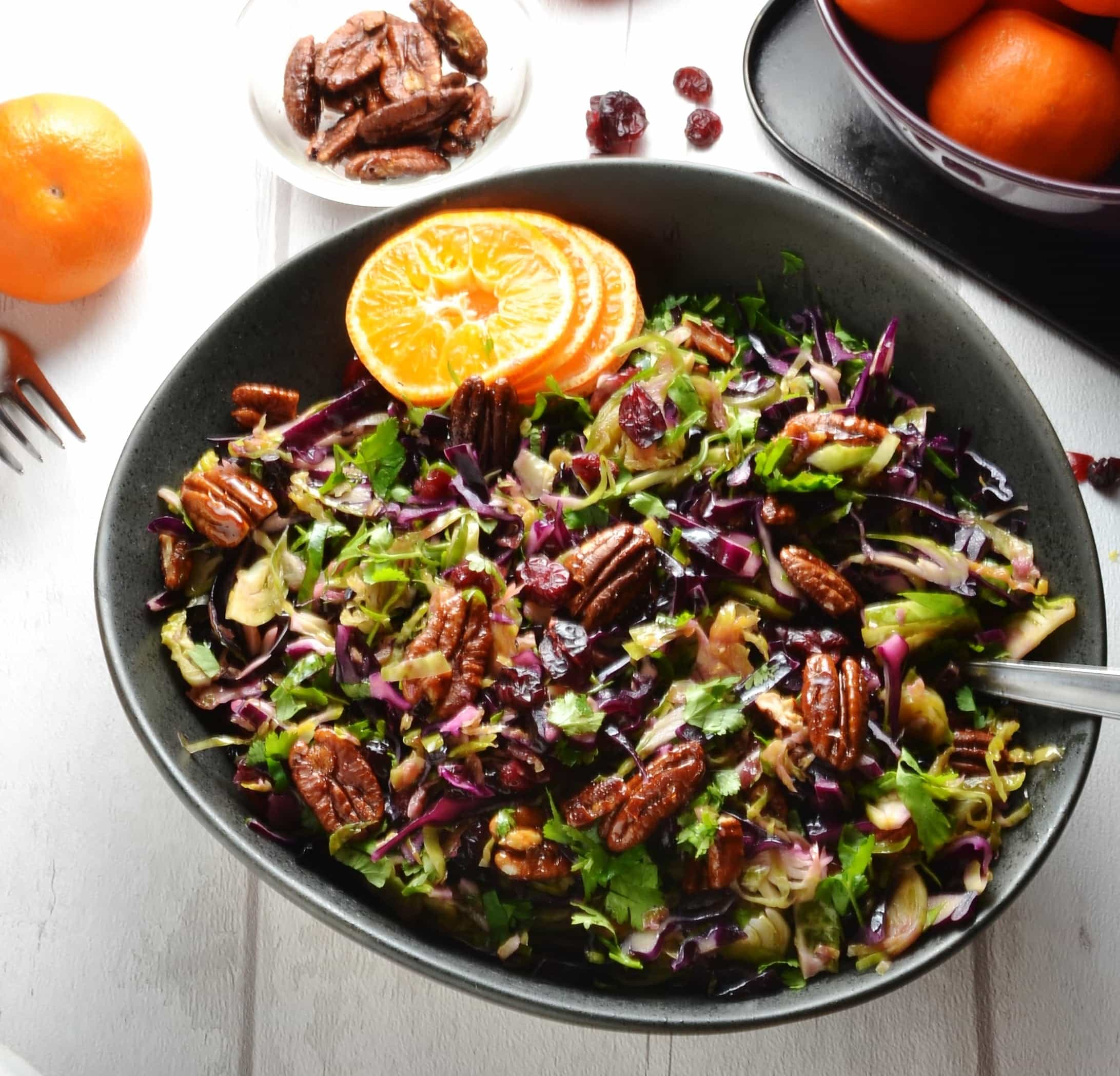 Top down view of Christmas slaw in black bowl with pecans and clementine in background.