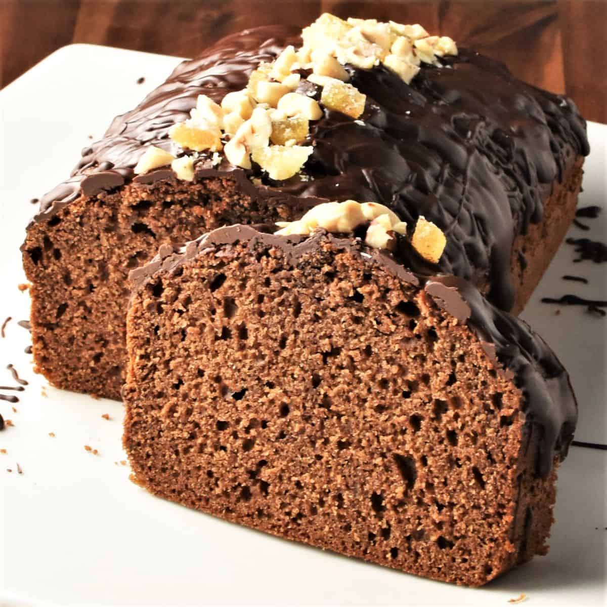 Side view of gingerbread loaf cake topped with chocolate and nuts.