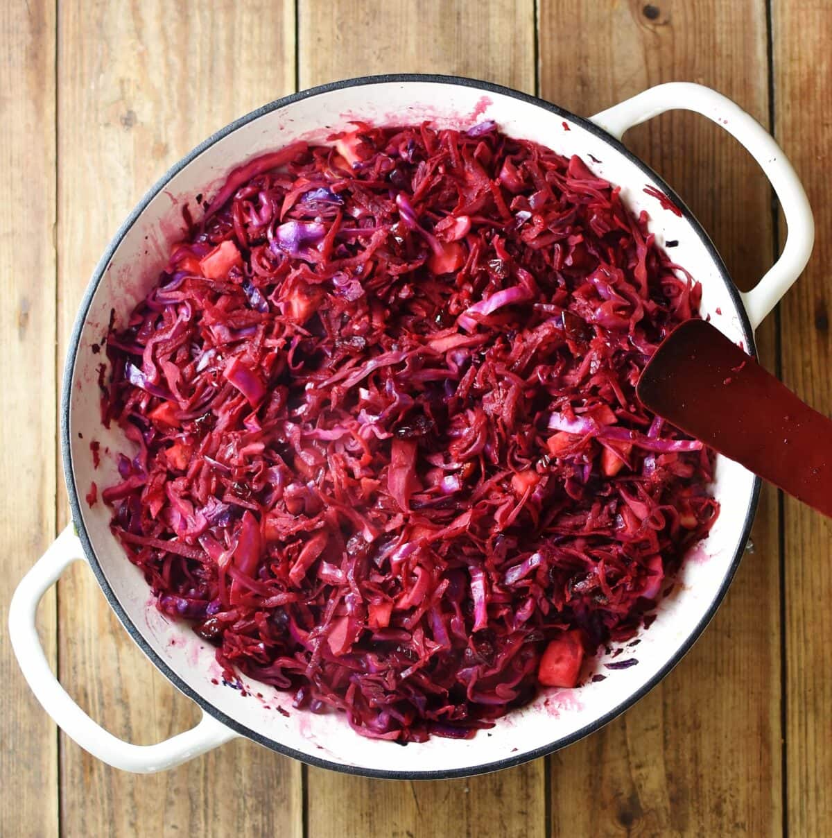 Braised red cabbage with red spatula in large white pan.