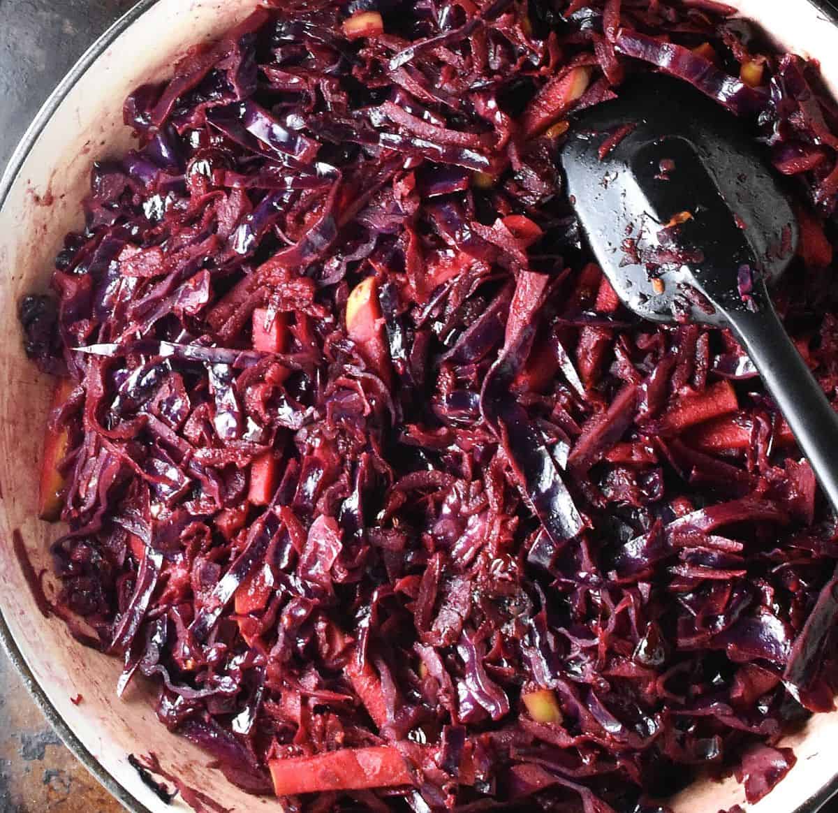 Top down view of ruby red braised purple cabbage in large shallow pan with black spoon.