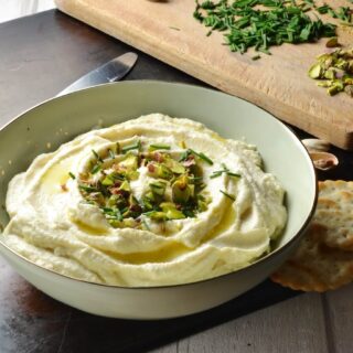 Close-up side image of Cauliflower Dip garnished with chives and pistachios in cream colour bowl.