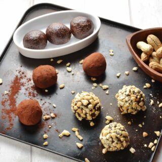 Side view of energy balls coated in cocoa and crushed nuts on top of dark tray.