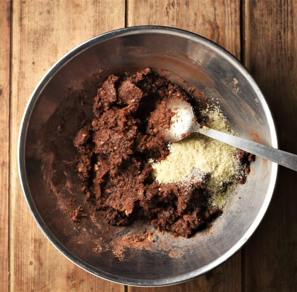 Chocolate quinoa mixture with ground almonds and large spoon in large metal bowl.