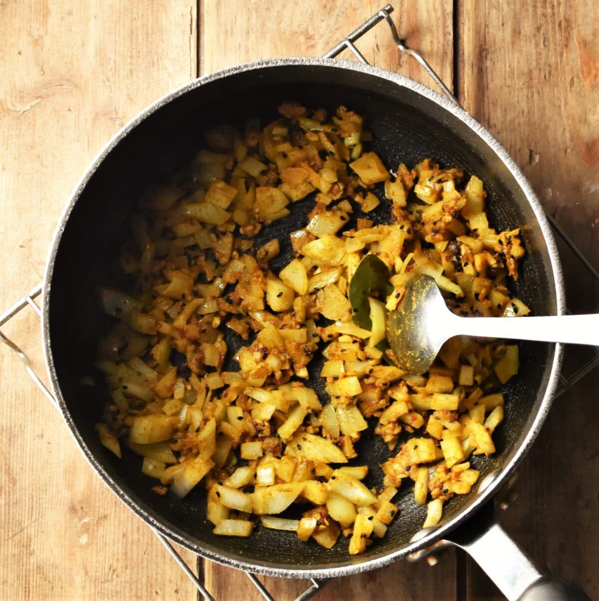 Chopped onions and spices in large pot with spoon.