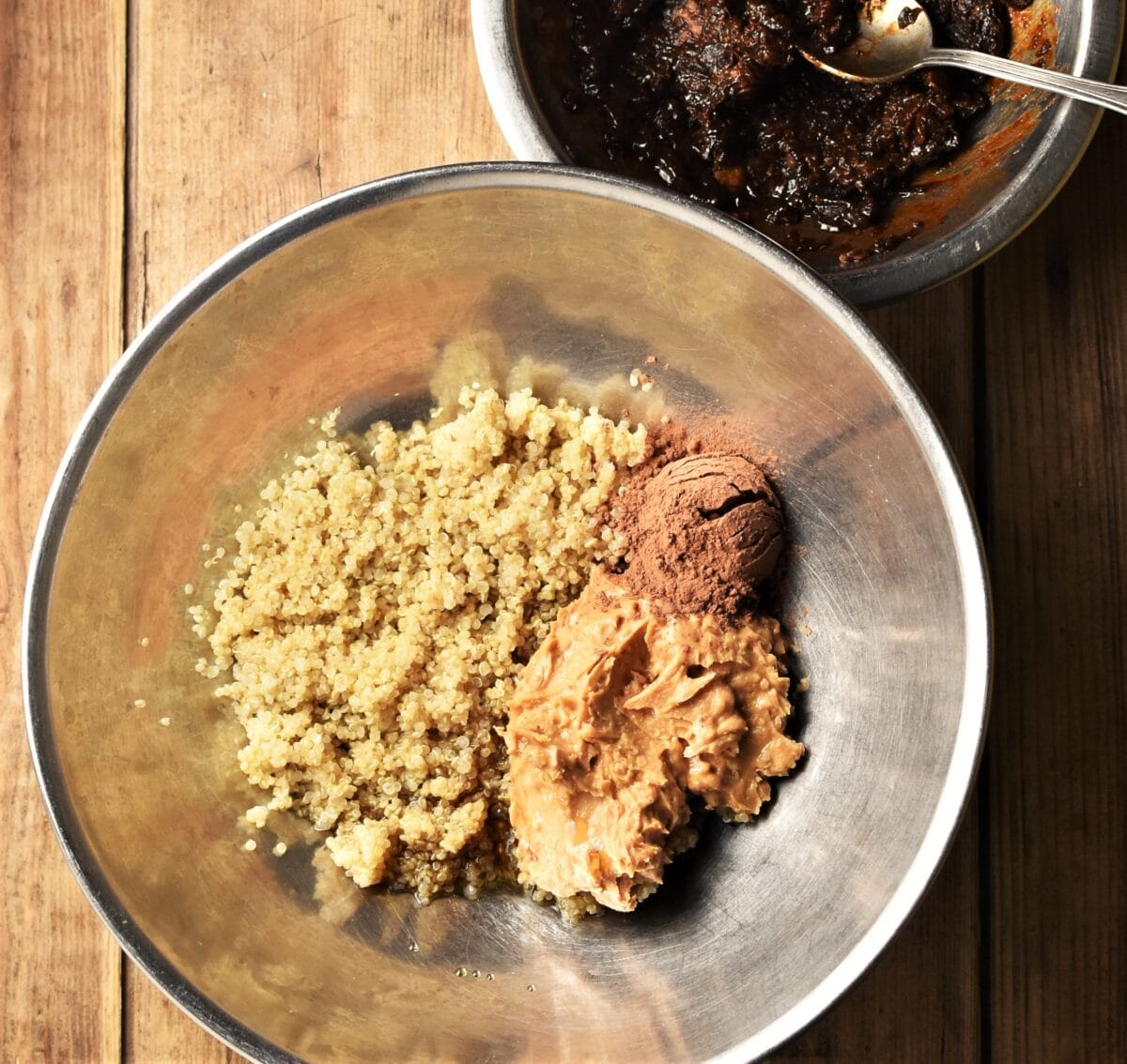 Cooked quinoa, peanut butter and cocoa in large metal bowl, with dates in small metal bowl in top right corner.