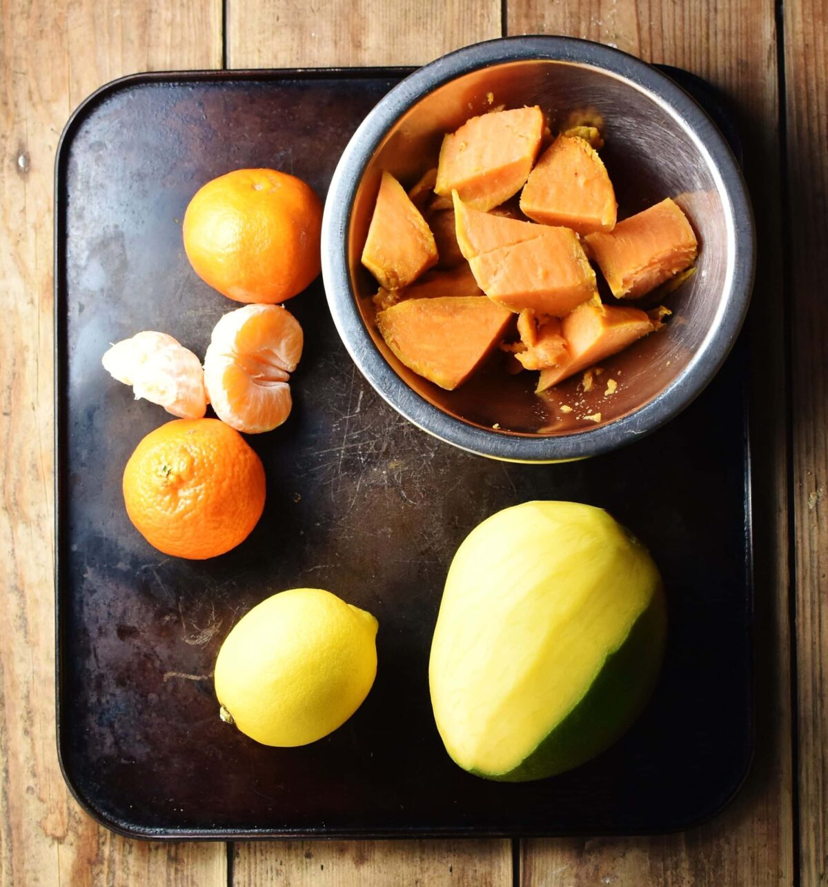 Tangerines, lemon, mango and chopped sweet potato in metal bowl.