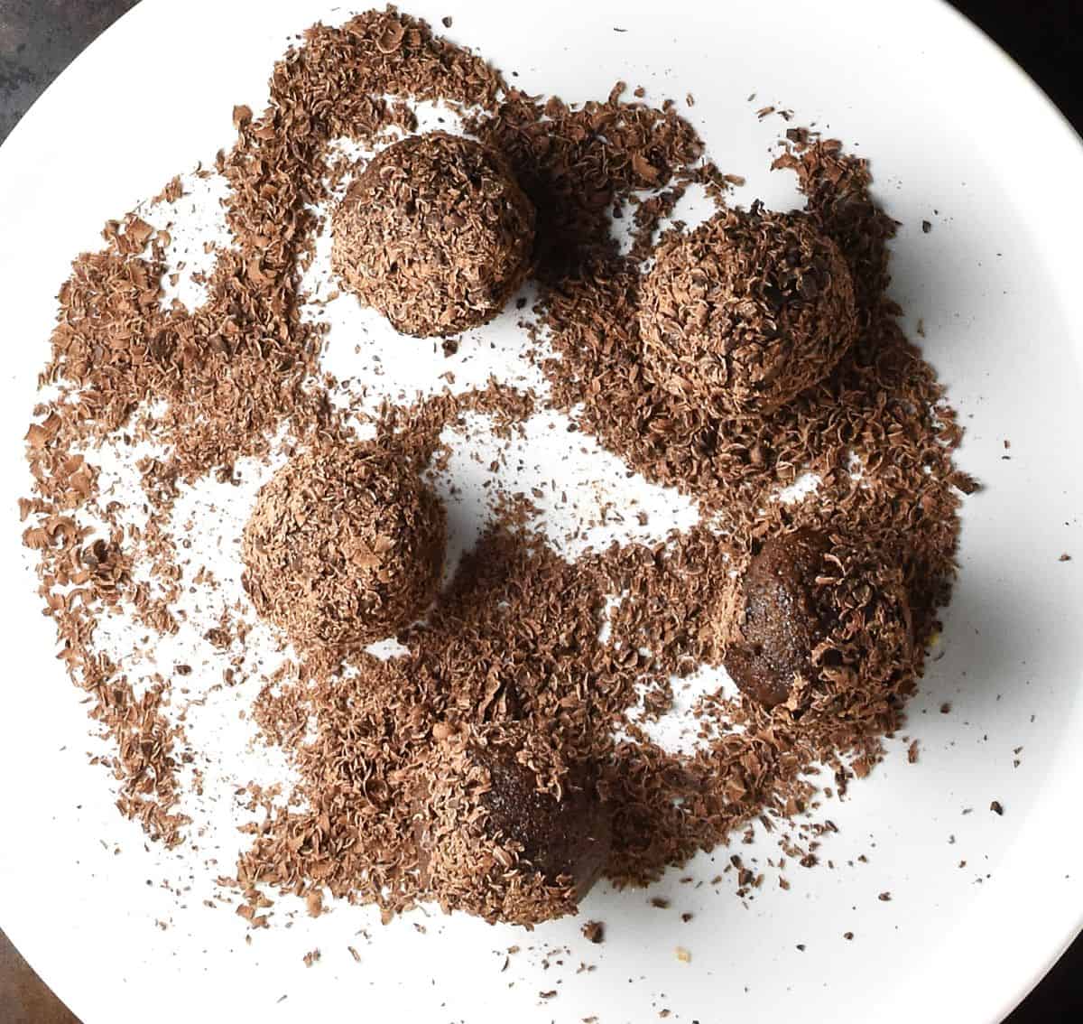 Top down view of energy balls coated in chocolate flakes on white plate.
