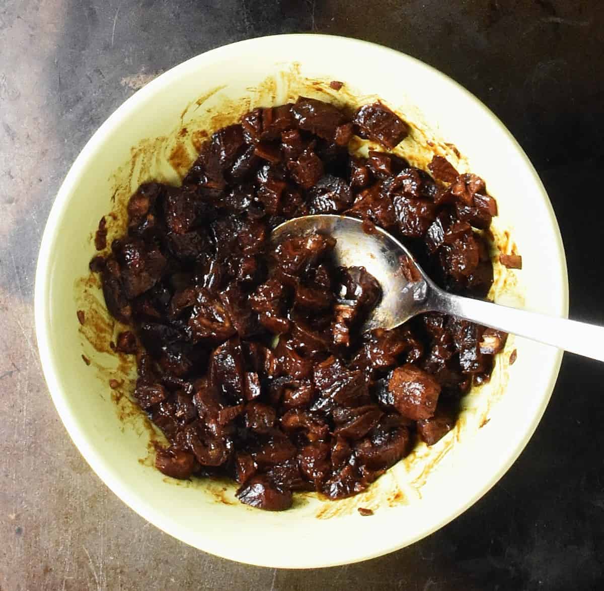 Chopped dates in yellow bowl with spoon.