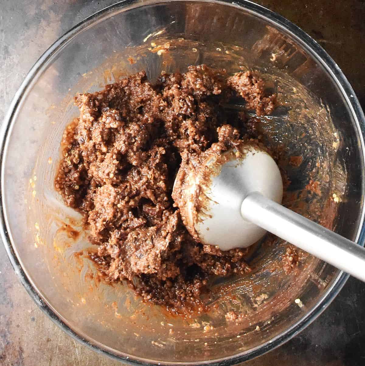 Top down view of quinoa protein ball mixture with immersion blender in glass bowl.
