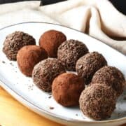 Side view of quinoa energy balls coated in cocoa and chocolate flakes on white oval plate.